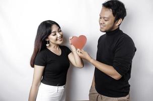 un joven asiático Pareja sonriente y participación rojo en forma de corazon papel, aislado por blanco antecedentes foto