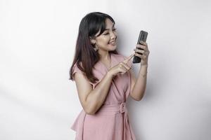 A portrait of a happy Asian woman dressed in pink and holding her phone, isolated by white background photo