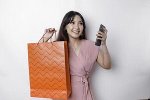 Portrait Asian happy beautiful young woman standing excited holding an online shopping bag and her smartphone, studio shot isolated on white background photo