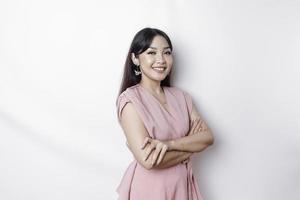 Portrait of a confident smiling Asian woman dressed in pink, standing with arms folded and looking at the camera isolated over white background photo