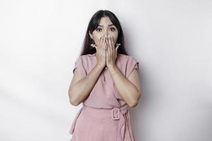 Surprised young Asian woman covering mouth with hands and staring at camera while standing against white background photo