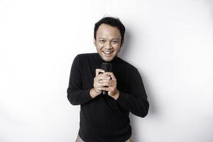 Portrait of carefree Asian man, having fun karaoke, singing in microphone while standing over white background photo