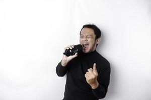 Portrait of carefree Asian man, having fun karaoke, singing in microphone while standing over white background photo