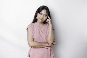 A thoughtful young woman dressed in pink blouse while looking aside, isolated by white background photo