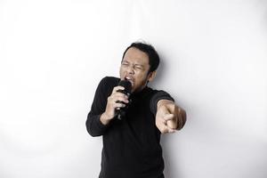 Portrait of carefree Asian man, having fun karaoke, singing in microphone while standing over white background photo