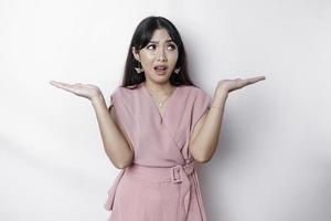 A thoughtful young Asian woman is wearing pink blouse holding her phone and looks confused, isolated by white background photo