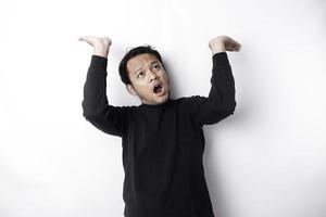 Shocked Asian man wearing black shirt pointing at the copy space on top of him, isolated by white background photo