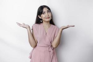 A thoughtful young Asian woman is wearing pink blouse holding her phone and looks confused, isolated by white background photo