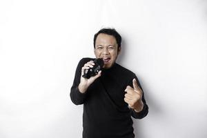 Portrait of carefree Asian man, having fun karaoke, singing in microphone while standing over white background photo