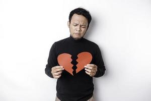 hermosa joven asiático hombre expresado su tristeza mientras participación roto corazón aislado en blanco antecedentes foto
