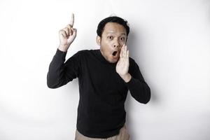 Shocked Asian man wearing black shirt pointing at the copy space on top of him, isolated by white background photo