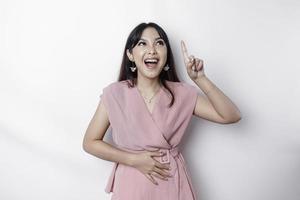 Starving Asian woman dressed in pink, pointing at the copy space on top of her, isolated by white background photo