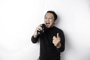 Portrait of carefree Asian man, having fun karaoke, singing in microphone while standing over white background photo