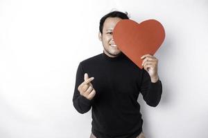 A portrait of a happy Asian man wearing a black shirt, holding a red heart-shaped paper isolated by white background photo