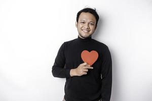 A portrait of a happy Asian man wearing a black shirt, holding a red heart-shaped paper isolated by white background photo