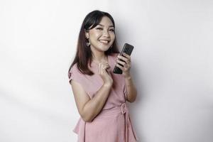 A portrait of a happy Asian woman dressed in pink and holding her phone, isolated by white background photo