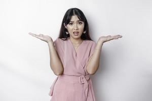 A thoughtful young Asian woman is wearing pink blouse holding her phone and looks confused, isolated by white background photo