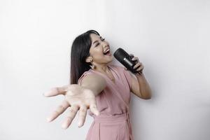 Portrait of carefree Asian woman, having fun karaoke, singing in microphone while standing over white background photo