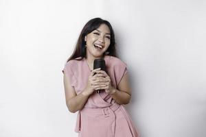 Portrait of carefree Asian woman, having fun karaoke, singing in microphone while standing over white background photo