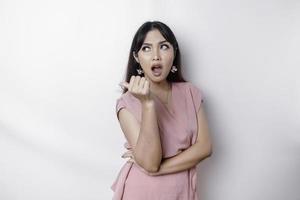 Questioned unaware young Asian pointing copy space beside her, look confused open mouth uncertain, being clueless, stand white background wear pink blouse photo