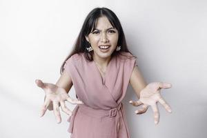 A dissatisfied young Asian woman looks at the camera posing on a white background, disgruntled girl with irritated face expressions show negative attitude concept image photo