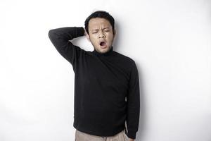 Portrait of sleepy attractive Asian man wearing a black shirt, feeling tired after night without sleep, yawning, covering opened mouth with palm photo