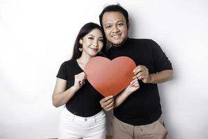 A young Asian couple smiling and holding red heart-shaped paper, isolated by white background photo