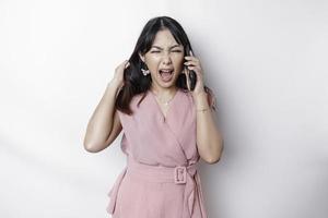 A dissatisfied young Asian woman dressed in pink, looks disgruntled with irritated face expressions holding her phone photo