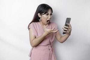 A dissatisfied young Asian woman dressed in pink, looks disgruntled with irritated face expressions holding her phone photo