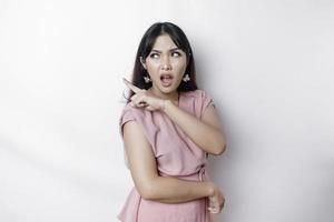 Questioned unaware young Asian pointing copy space beside her, look confused open mouth uncertain, being clueless, stand white background wear pink blouse photo