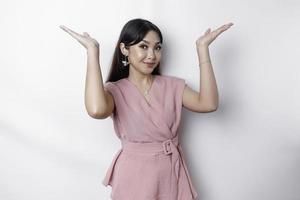 Excited Asian woman dressed in pink, pointing at the copy space on top of her, isolated by white background photo