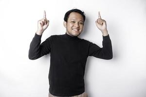 Excited Asian man wearing black shirt pointing at the copy space on top of him, isolated by white background photo