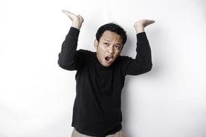 Shocked Asian man wearing black shirt pointing at the copy space on top of him, isolated by white background photo