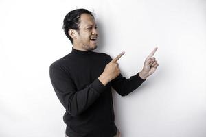 Excited Asian man wearing black shirt pointing at the copy space beside him, isolated by white background photo