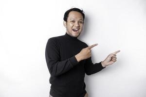 Excited Asian man wearing black shirt pointing at the copy space beside him, isolated by white background photo