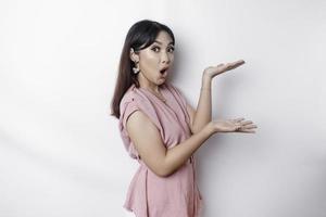 Shocked Asian woman dressed in pink, pointing at the copy space on beside her, isolated by white background photo