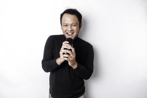 Portrait of carefree Asian man, having fun karaoke, singing in microphone while standing over white background photo