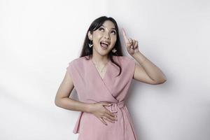 Starving Asian woman dressed in pink, pointing at the copy space on top of her, isolated by white background photo