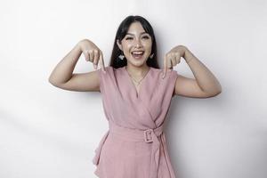 Excited Asian woman dressed in pink, pointing down at the copy space, isolated by white background photo