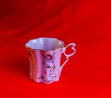 porcelana rosado taza de un raro forma es hecho en el checo república. un taza con un romántico modelo en un rojo antecedentes. foto