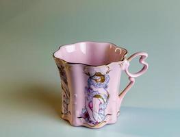 Porcelain pink cup of an unusual shape is made in the Czech Republic. A cup with a romantic pattern on a white background. photo