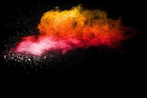 Red yellow powder explosion cloud on black background. Freeze motion of red yellow color dust particles splashing. photo