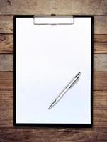 white paper clipboard on wood background with pen photo