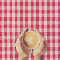 Man hand holding cup coffee on red and white fabric. photo