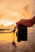 A Camera with hands photographs a Balinese woman doing a gymnastic movement on a black shirt near the beach photo