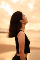 un hermosa asiático mujer en negro ropa es disfrutando el belleza de el playa con un sonriente expresión en su cara mientras en vacaciones foto