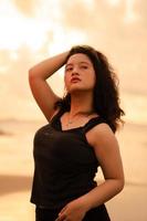 an Asian woman posing with her hands raised and touching her black hair passionately on the beach photo