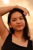 hermosa asiático mujer con un negro camisa y negro pelo sonriente con suave piel cerca el playa foto
