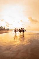 un grupo de asiático adolescentes en camisas corriendo con su amigos con muy alegre expresiones en el playa foto