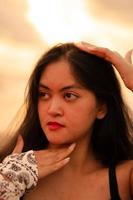 An Asian woman with long black hair poses with her hands while enjoying the view of the beach photo